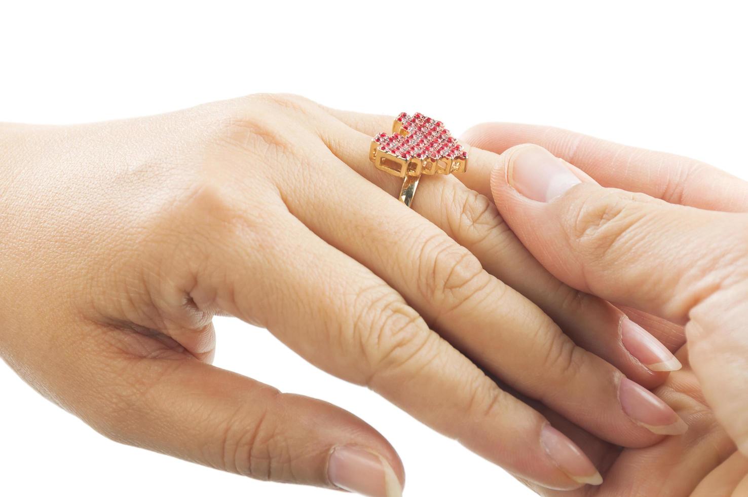 el primer plano de la mano del hombre está poniendo un anillo con forma de corazón en el dedo anular de la mujer sobre fondo blanco foto