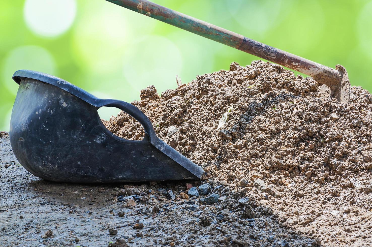 Hoe and clam-shell shaped bucket and soil mound over green bokeh background photo