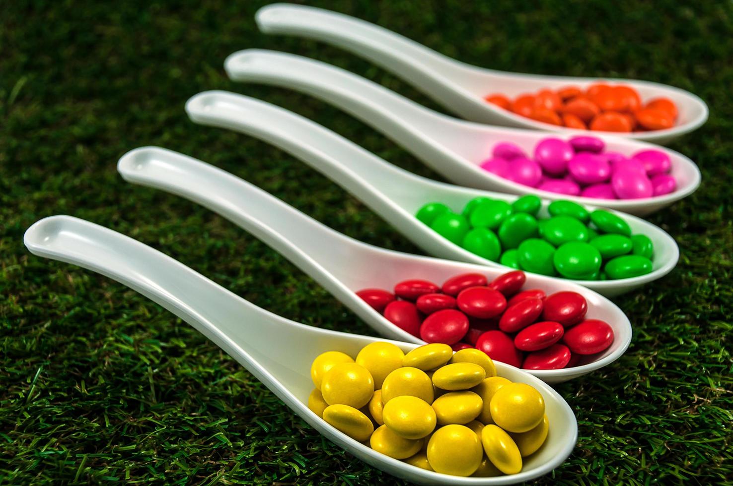Colorful chocolate candy served on spoons with green grass background photo