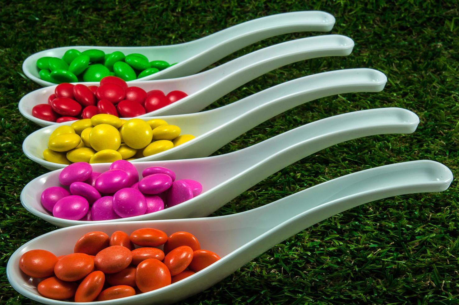 Colorful chocolate candy served on spoons with green grass background photo