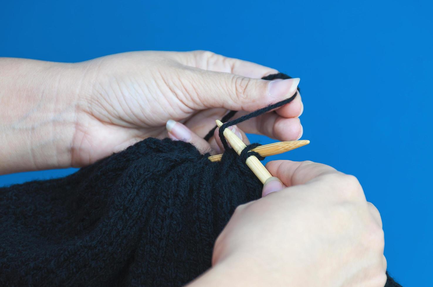 Woman's hands is making black hat knitting over light blue background photo