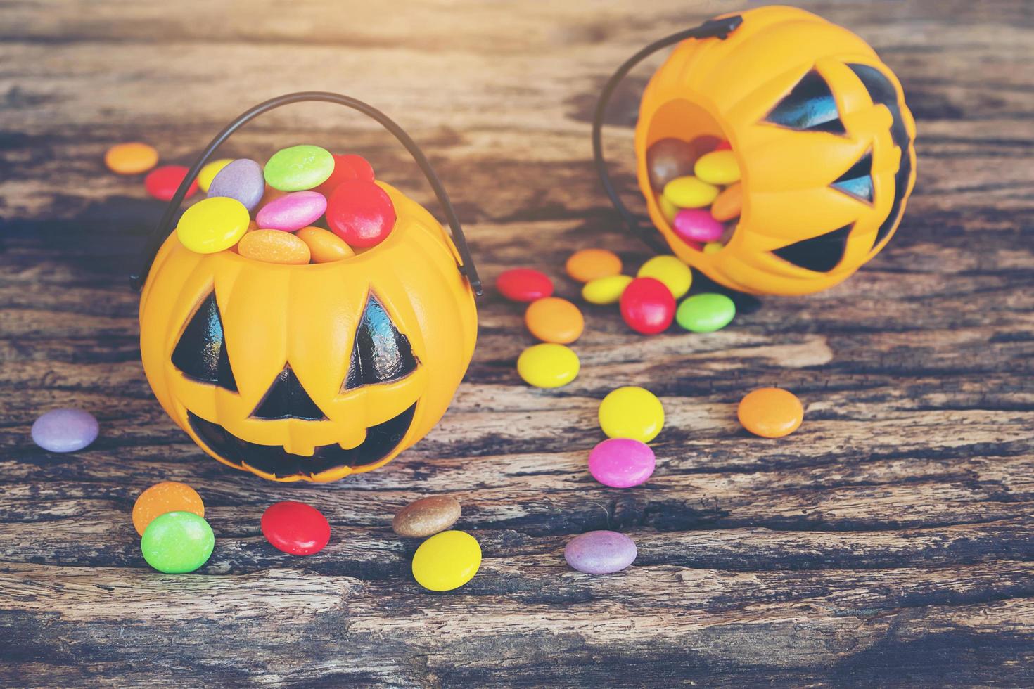 Halloween pumpkin face buckets with colorful candy inside on old wooden texture photo