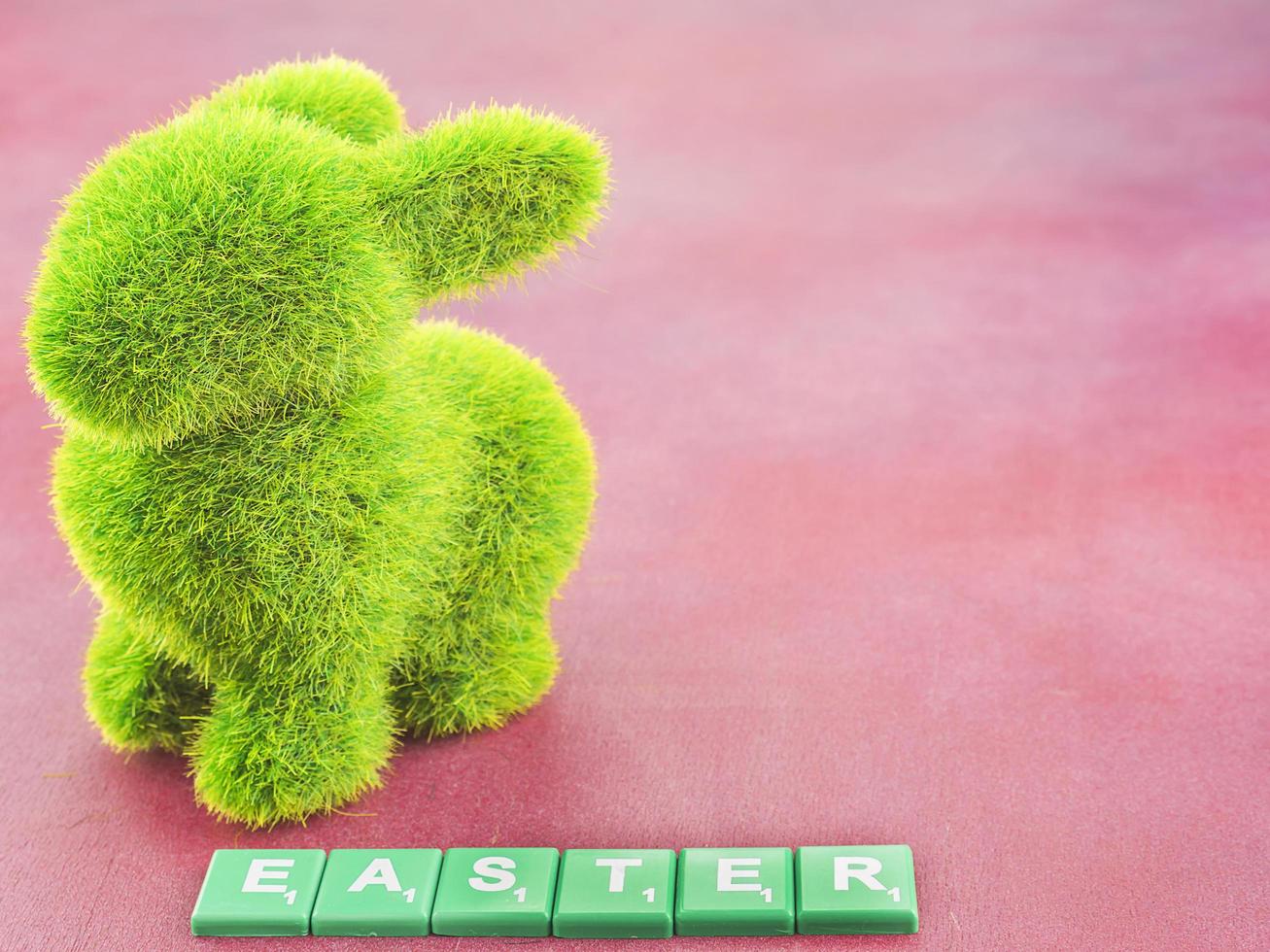Artificial green grass rabbit and Easter word over pink background photo