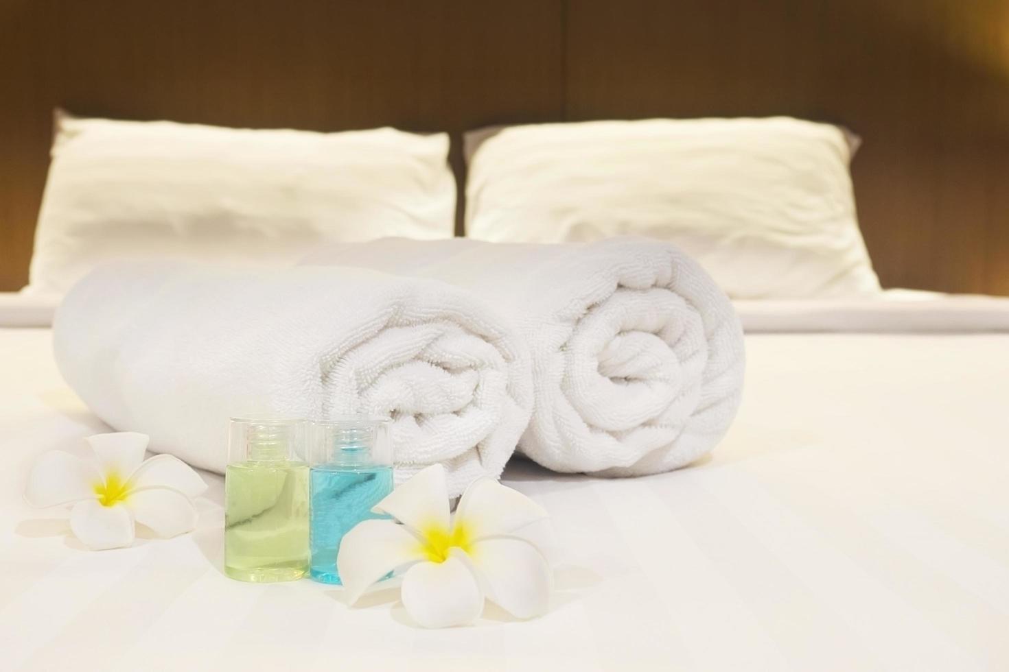 Hotel towel with flower and shampoo and soap bottle set on white bed photo