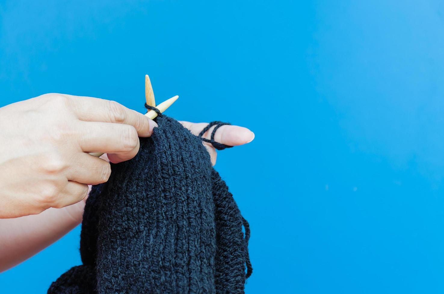 Woman's hands is making black hat knitting over light blue background photo