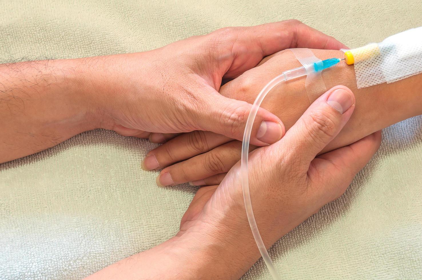 Man holding woman, patient, hand with a tube of medicine injection on a bed in a hospital photo