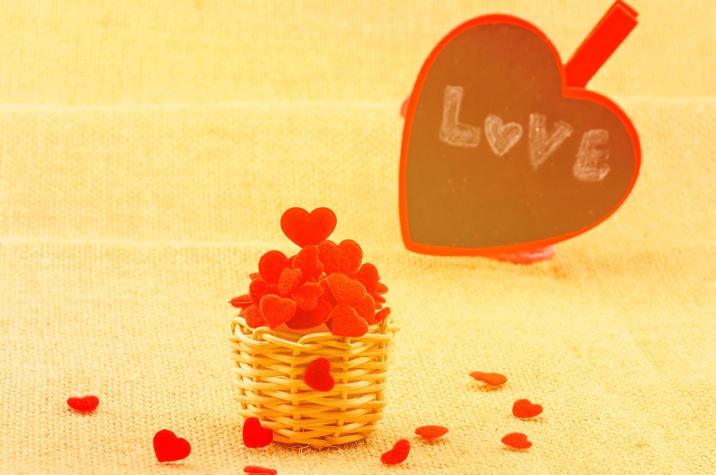 Warm color tone of hearts in small wooden weave basket and a love word on a heart board putting on the sack fabric. photo