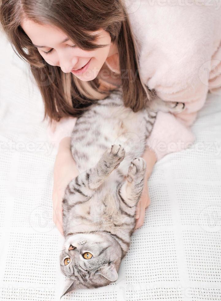 young woman playing with her tabby cat lying on a bed. stroking pet gently, friendship and love. vertical shot. photo