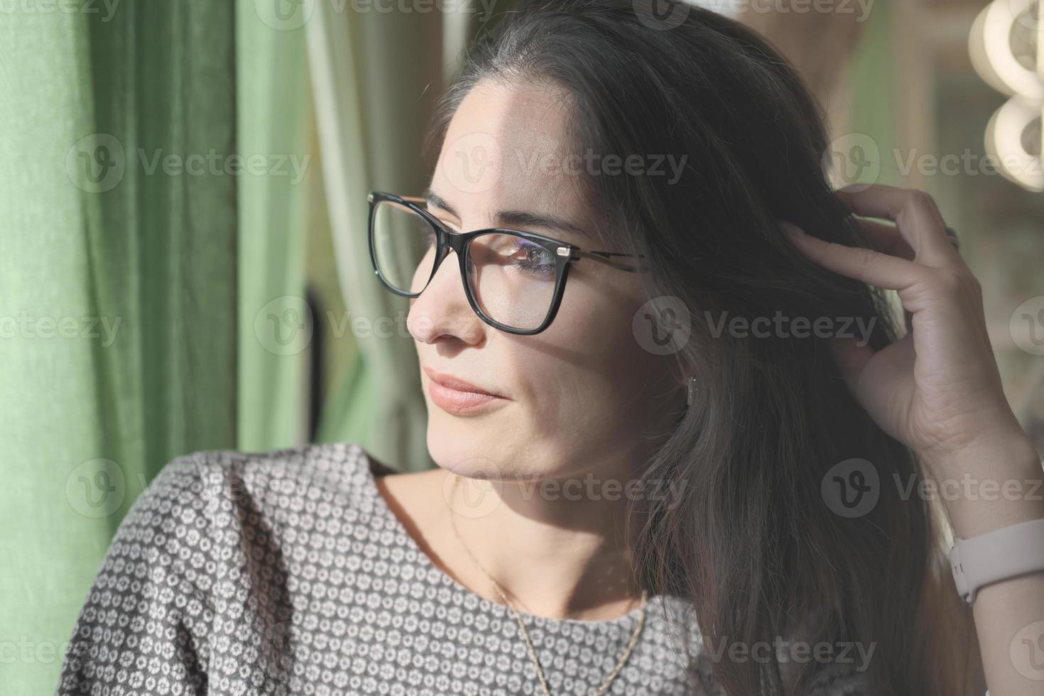 mujer asiática o de oriente medio con anteojos mirando a un lado y tocándose el pelo. descansar o descansar en la oficina, disfrutar del sol. hermosa mujer tranquila y pensativa. foto