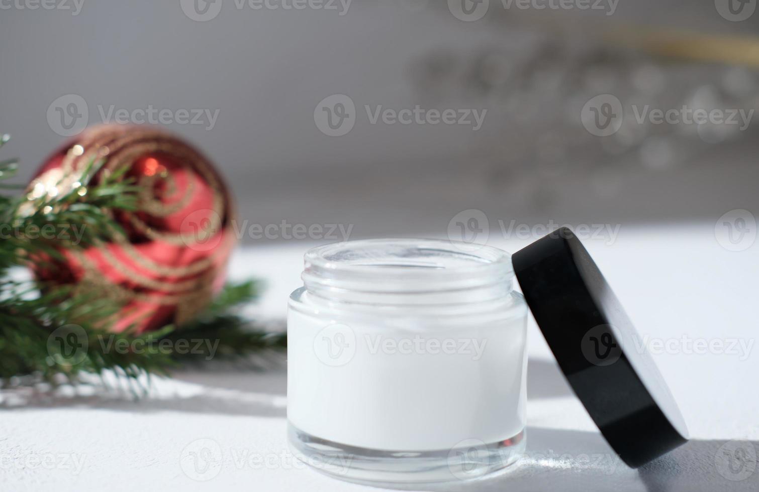 crema facial en frasco blanco junto a la decoración navideña, venta de año nuevo o regalo de vacaciones para mujeres. cuidado de la piel y la cara sensible, cosmético de protección contra el frío foto