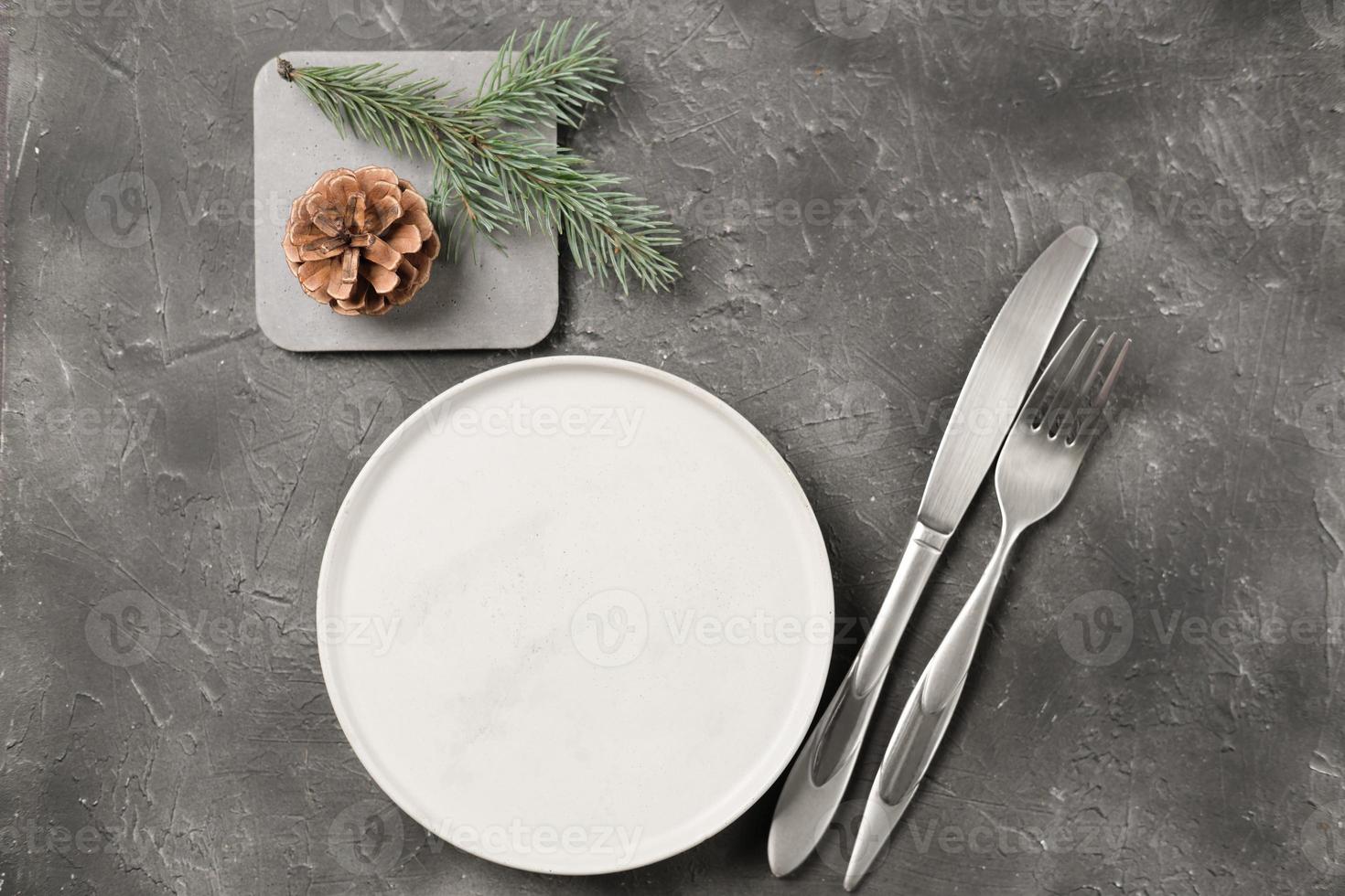 empty plate with silverware and christmas tree branch and cone on grey table. copy space. table setting template for new year or christmas menu. restaurant menu mock up. top view photo