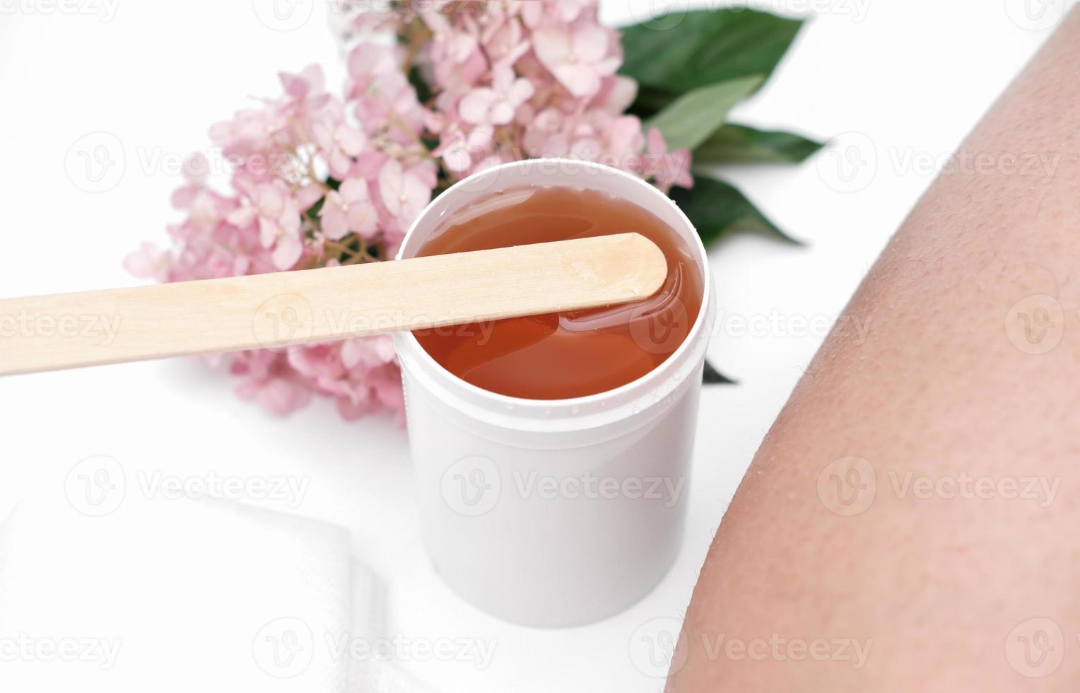 sugaring paste and spatula next to female leg. flowers on a background. depilation at home, skin and body care. hair removing. photo