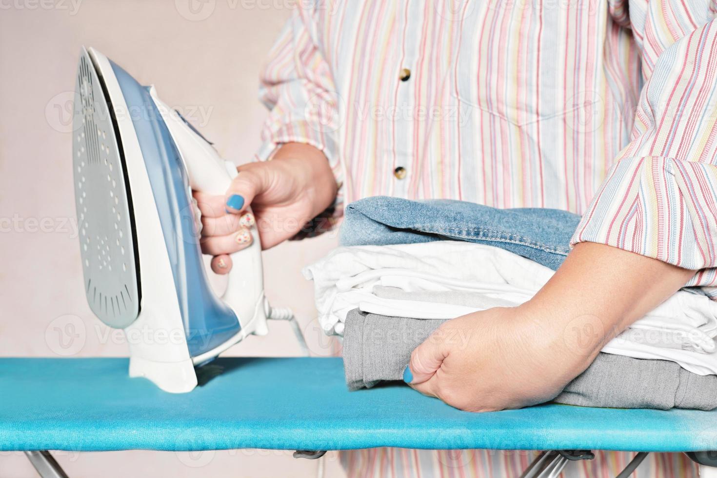 pila de ropa y mujer con hierro. trabajo a domicilio, tareas domésticas, concepto de limpieza. Ropa textil azul gris blanca. foto