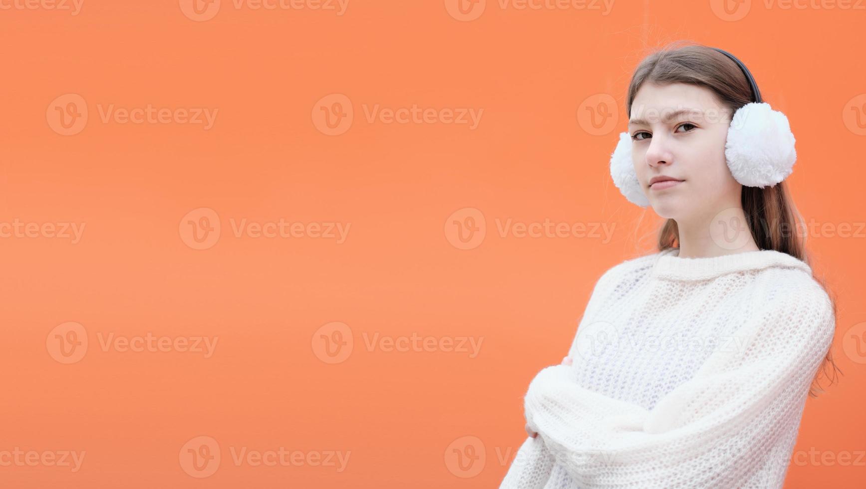 Fashionable caucasian teenager girl wearing white earmuffs with sweater and standing against orange background. hipster teen. generation z photo