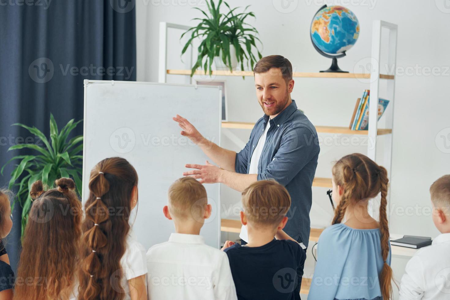 Explaining lesson and using board. Group of children students in class at school with teacher photo