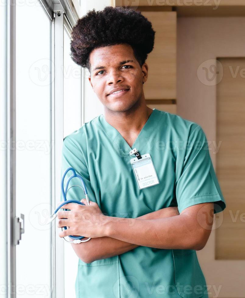 hombre negro médico de pie con los brazos cruzados mirando a la cámara sonriendo, retrato. feliz trabajador de ocupación médica profesional con un estetoscopio brinda servicios de consulta y tratamiento en el hospital foto