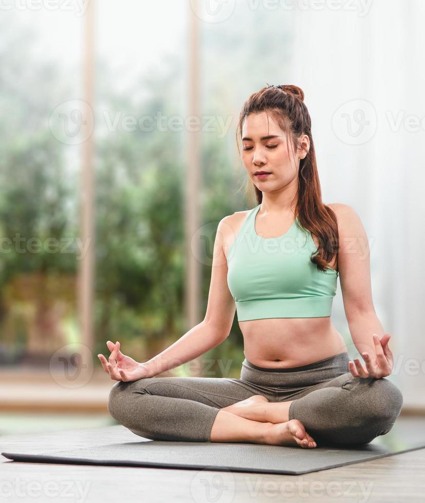 Closed eyes young Asian woman sits on an exercise mat to practice meditation isolated on a blurred background. copy space. Clam and relaxation concept. photo