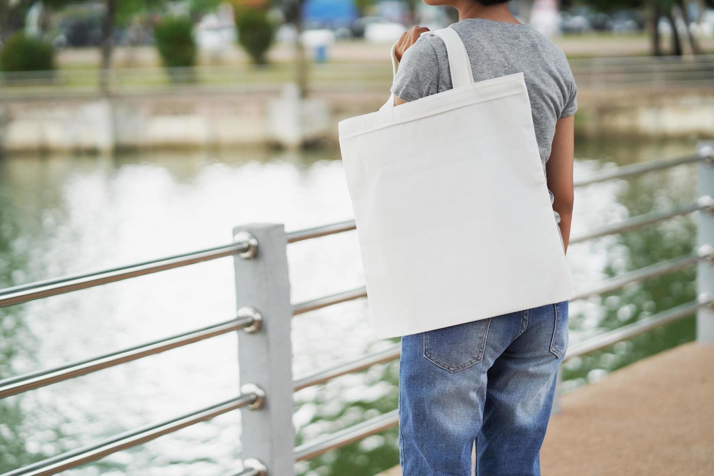 mujer hipster sosteniendo una bolsa de mano blanca para una plantilla en blanco simulada foto