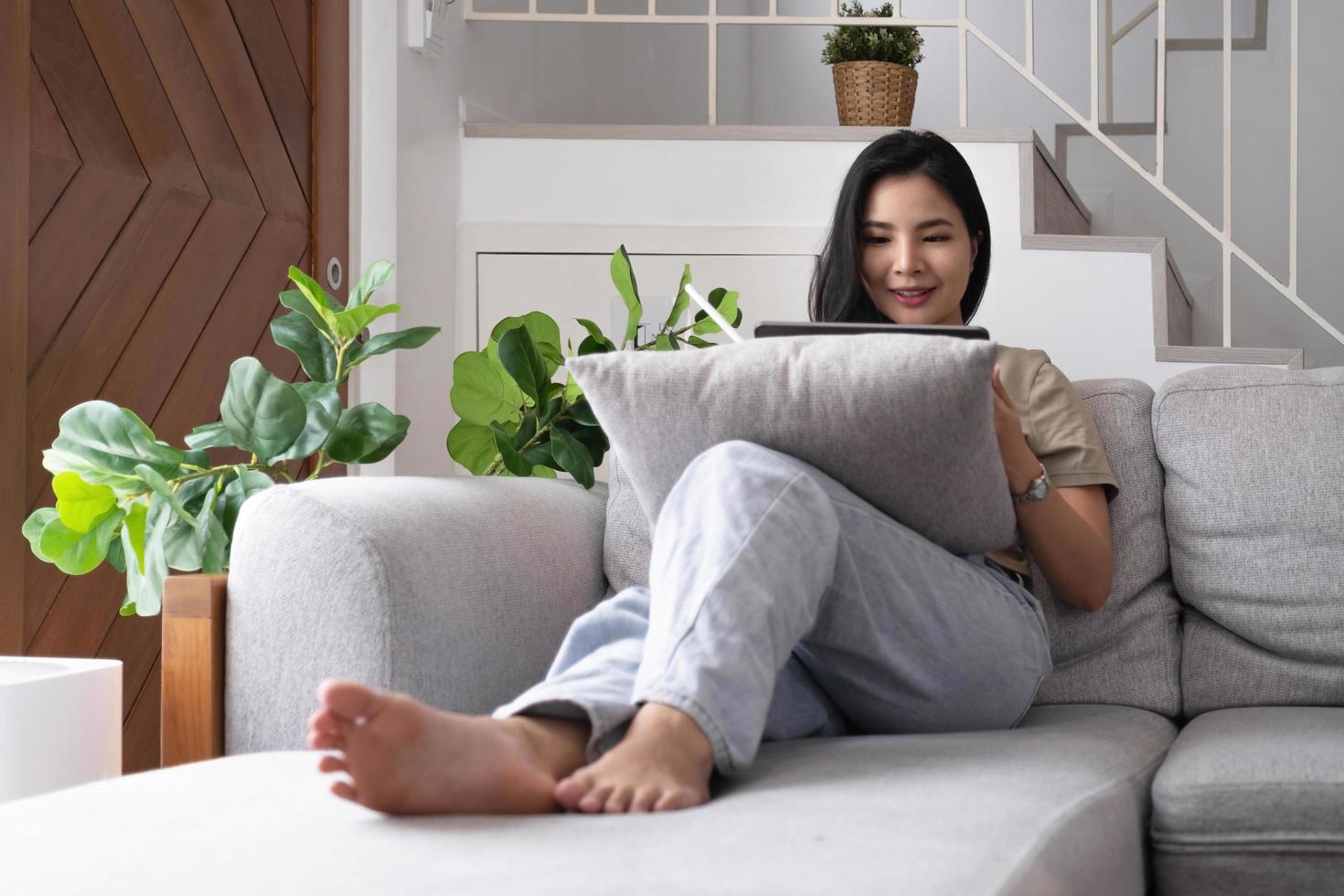 Attractive smiling young asian  woman relaxing on a leather couch at home, working on laptop computer. photo