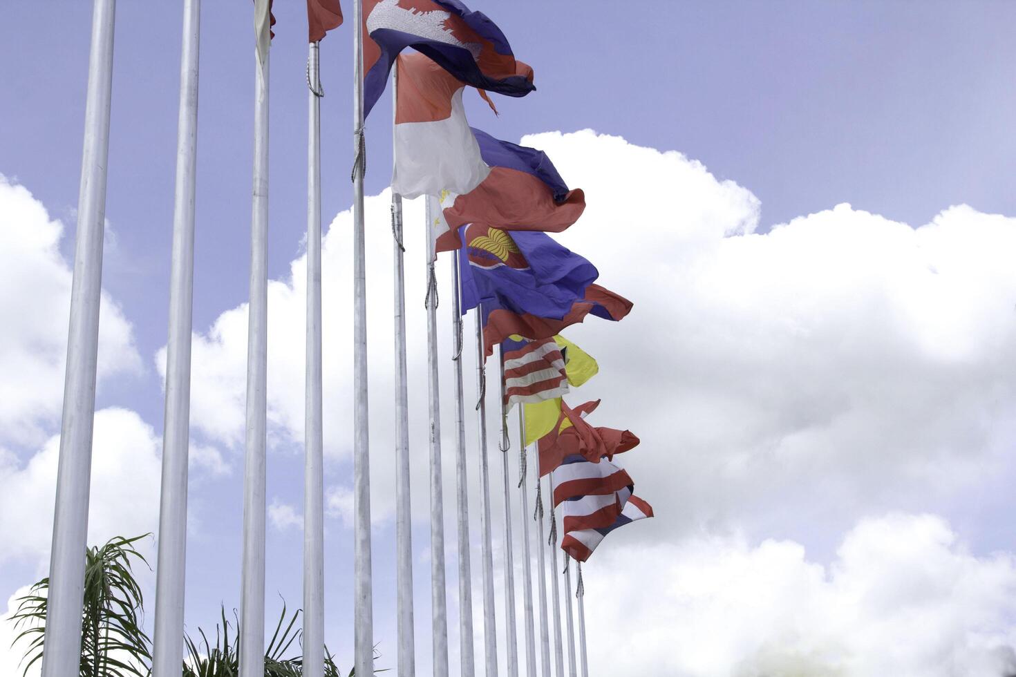 muchas de las banderas de la asean en los coloridos colores soplados por la fuerza del viento ondeando en un poste frente a un hotel en tailandia sobre un fondo con nubes y cielos azules. foto