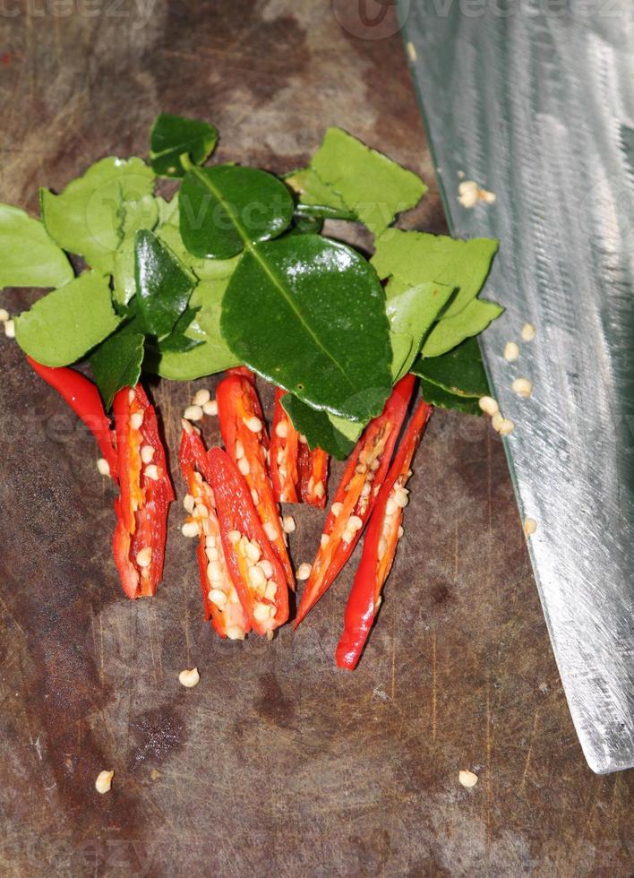 Preparation of sliced red peppers and green kaffir lime leaves on a wooden cutting board for cooking in a rural roadside restaurant in Thailand. photo