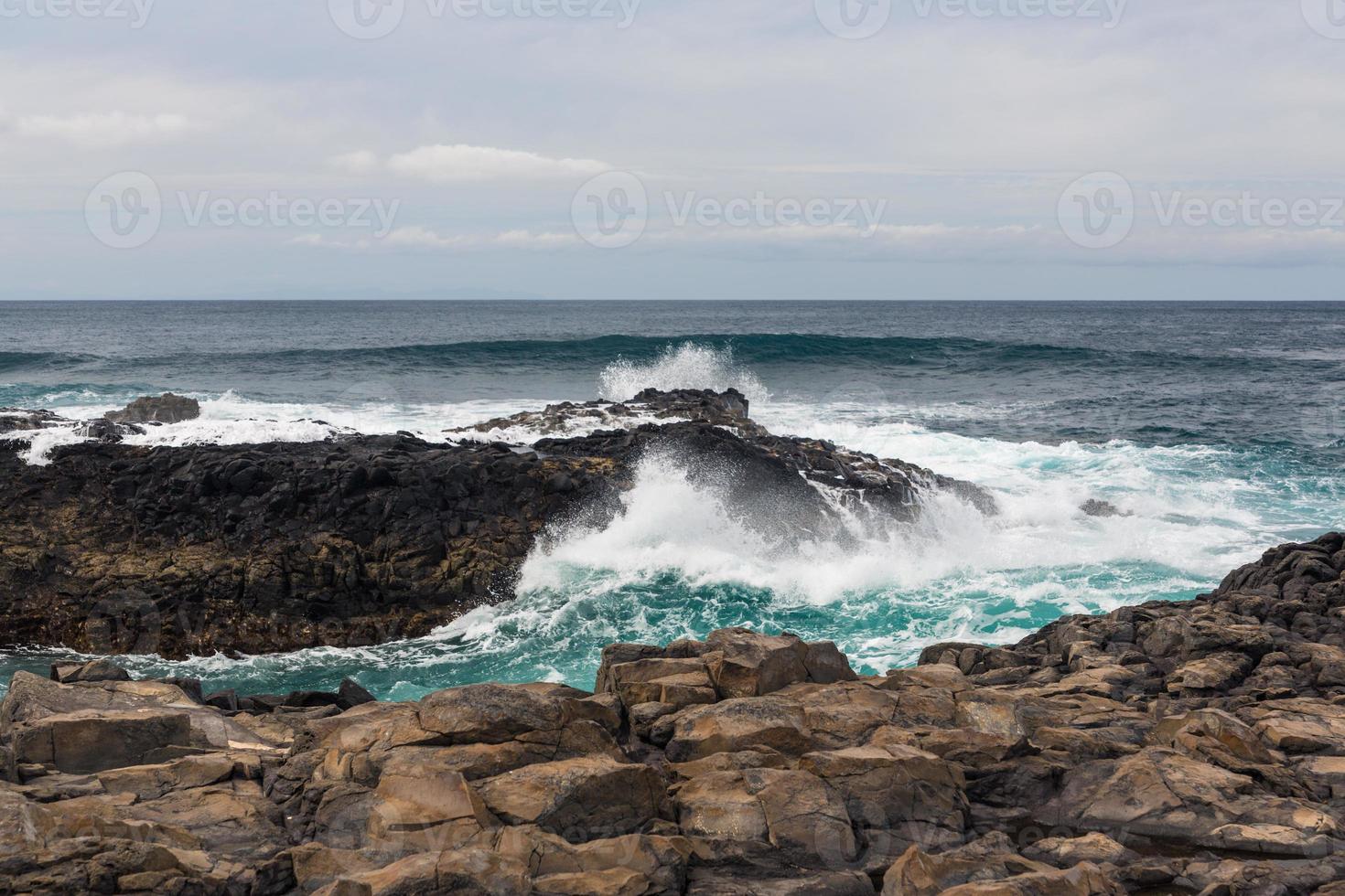 Turbulent ocean waves with white foam beat coastal stones photo