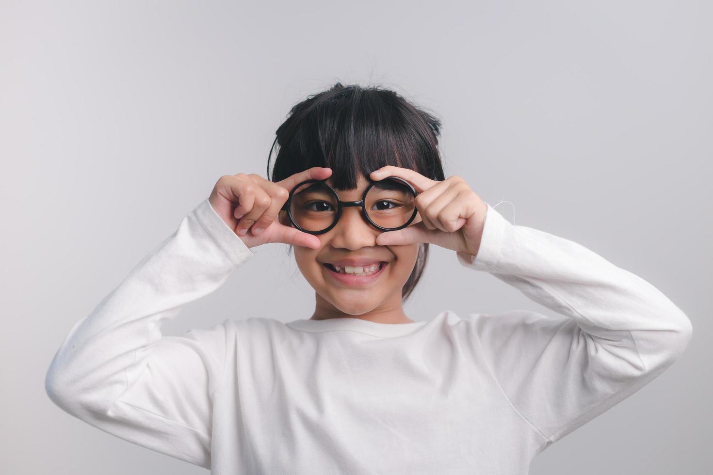 cute little preschooler girl isolated on grey studio background wear glasses look at camera, small child try spectacles at opticians, kid eyesight correction treatment concept photo