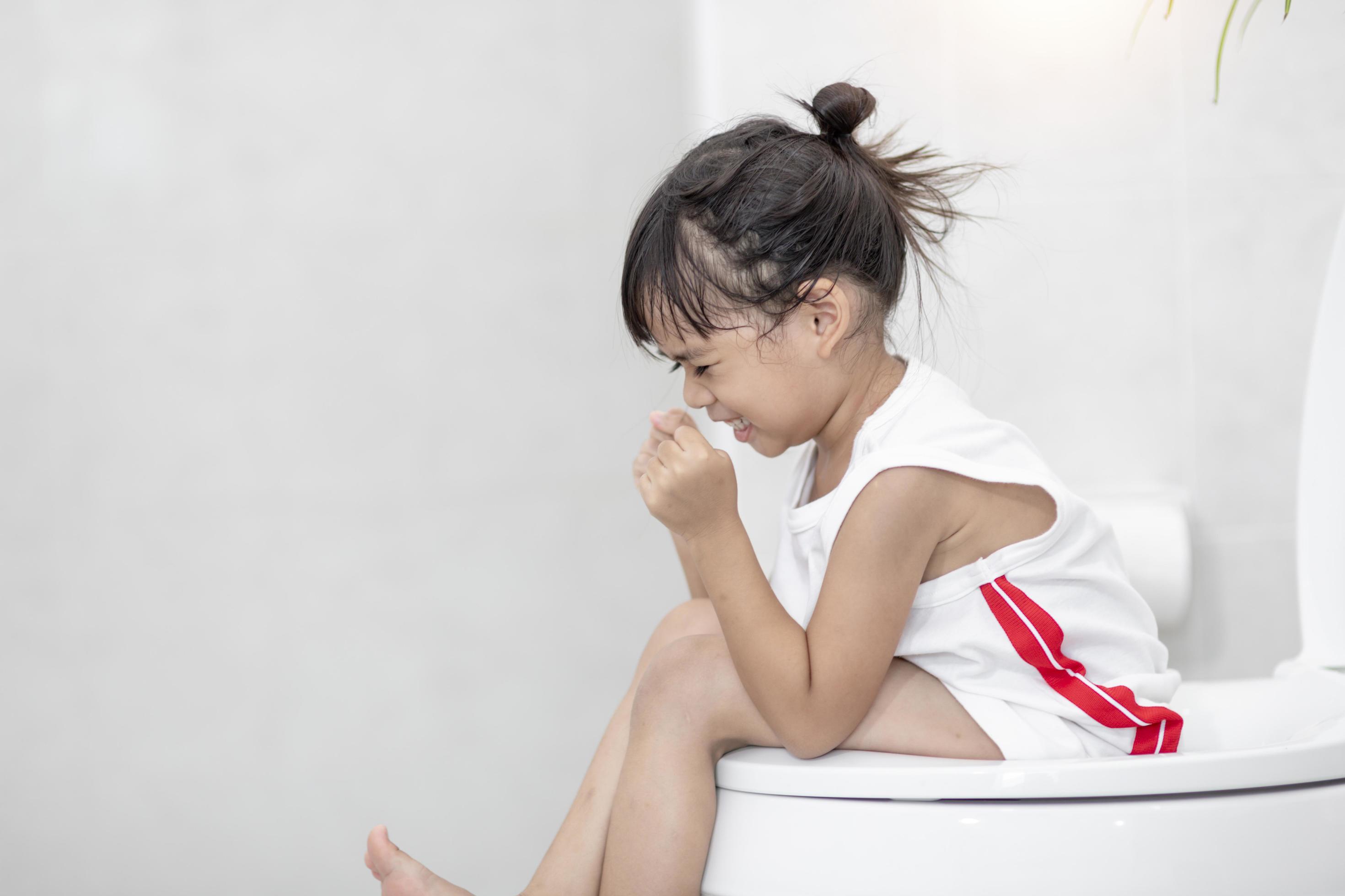 The little girl is sitting on the toilet suffering from constipation or