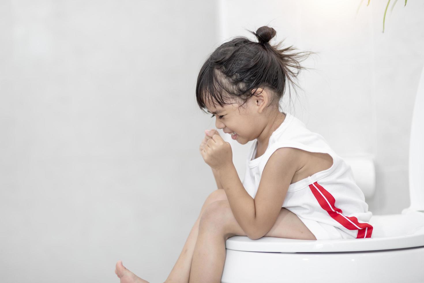 The little girl is sitting on the toilet suffering from constipation or hemorrhoid. photo