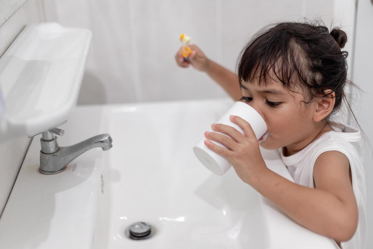 Little cute baby girl cleaning her teeth with a toothbrush in the bathroom photo