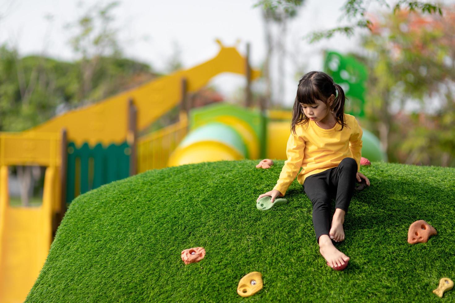 Cute Asian girl having fun trying to climb on artificial boulders at schoolyard playground, Little girl climbing up the rock wall, Hand Eye Coordination, Skills development photo