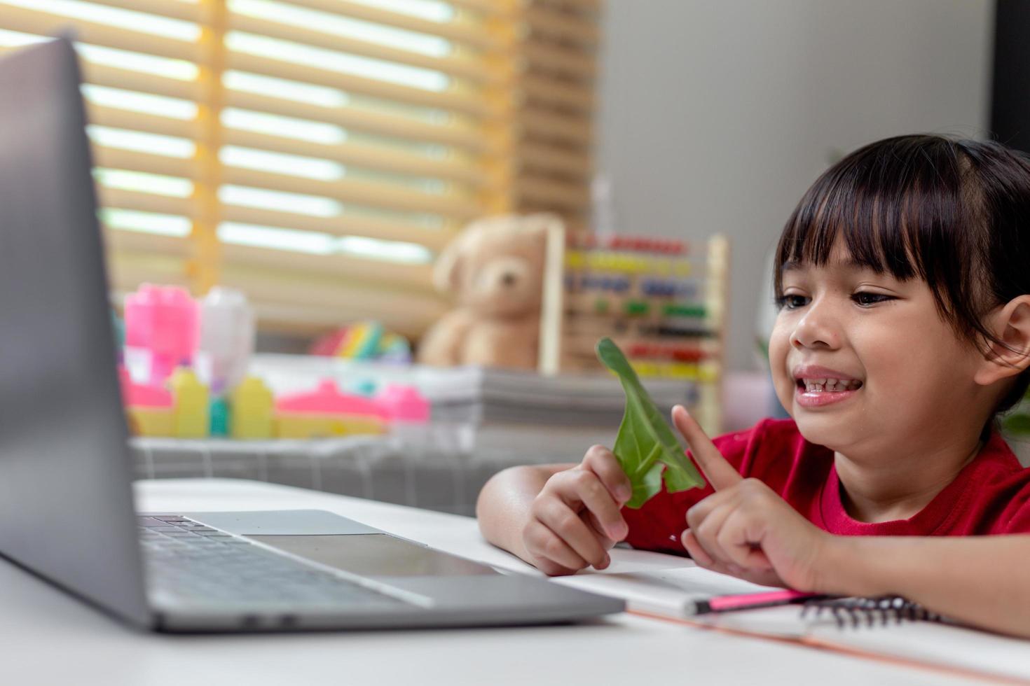 tiempo de aprender. una colegiala interesada en el auricular se sienta en el escritorio de su casa y mira la lección de video educativo. curiosa niña en edad escolar pequeña piensa en la pregunta del maestro selecciona la respuesta correcta en la pantalla del portátil foto