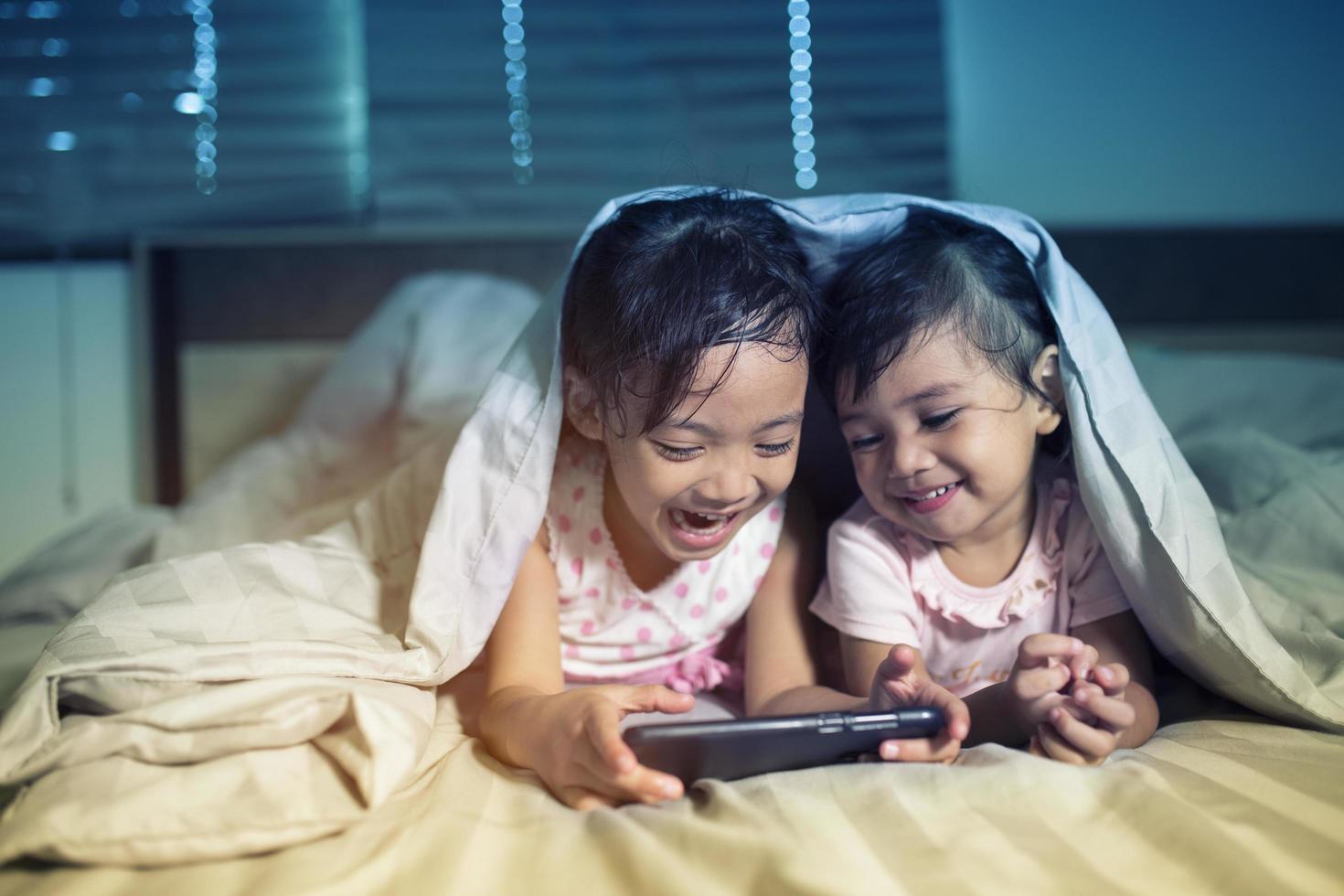 Cute girl looking at his younger sister who is playing a game on a smart phone on bed photo