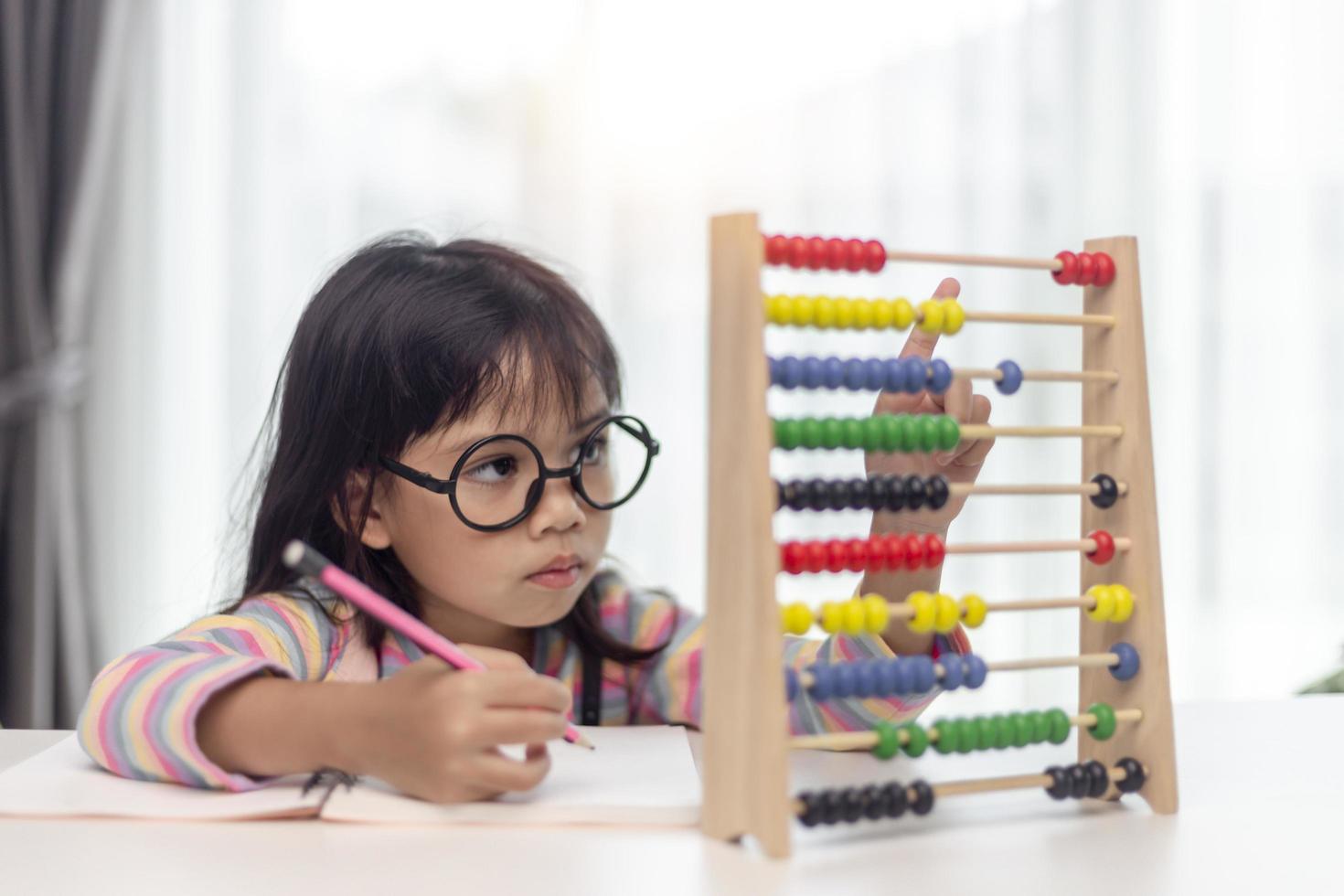 A young cute Asian girl is using the abacus with colored beads to learn how to count at home photo