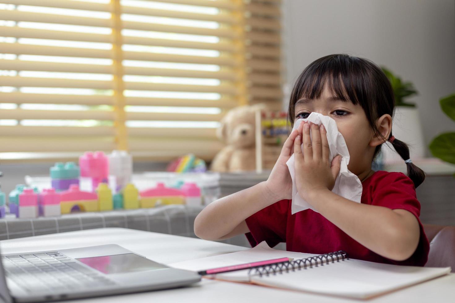 Unhealthy kid blowing nose into tissue, Child suffering from running nose or sneezing, A girl catches a cold when season change, childhood wiping nose with tissue photo