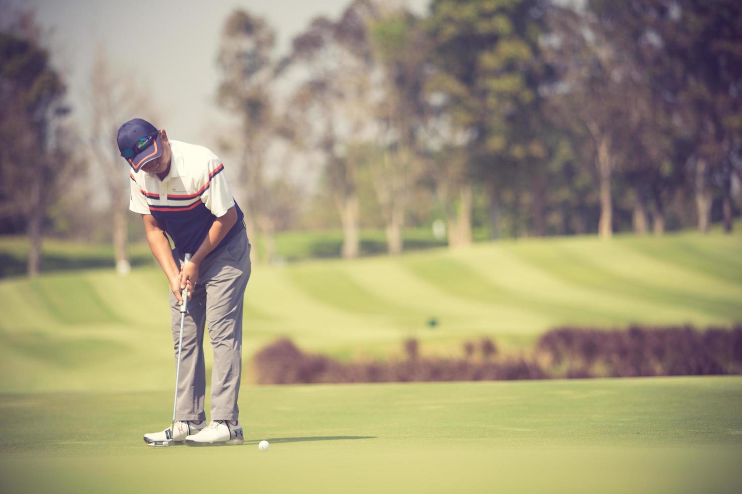 Golf player at the putting green hitting ball into a hole.Vintage color photo