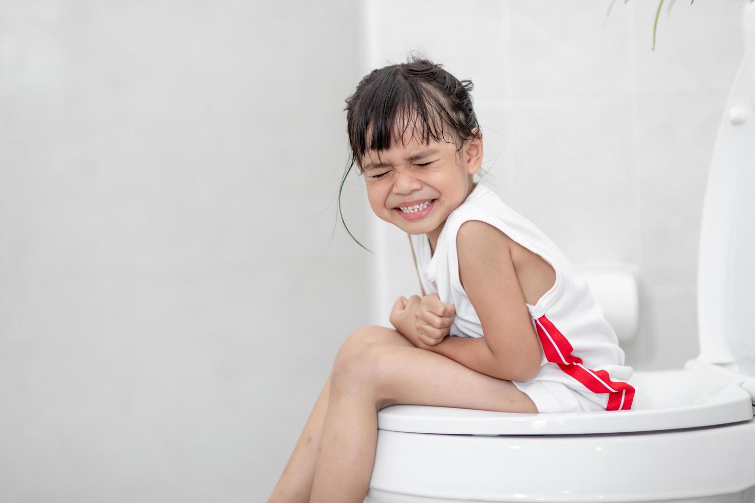 The little girl is sitting on the toilet suffering from constipation or hemorrhoid. photo