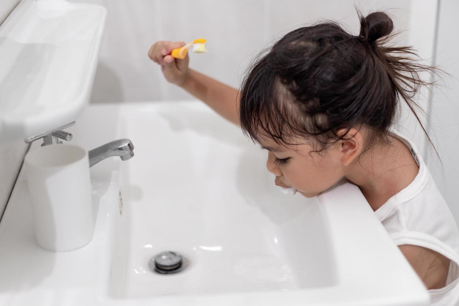 Little cute baby girl cleaning her teeth with a toothbrush in the bathroom photo