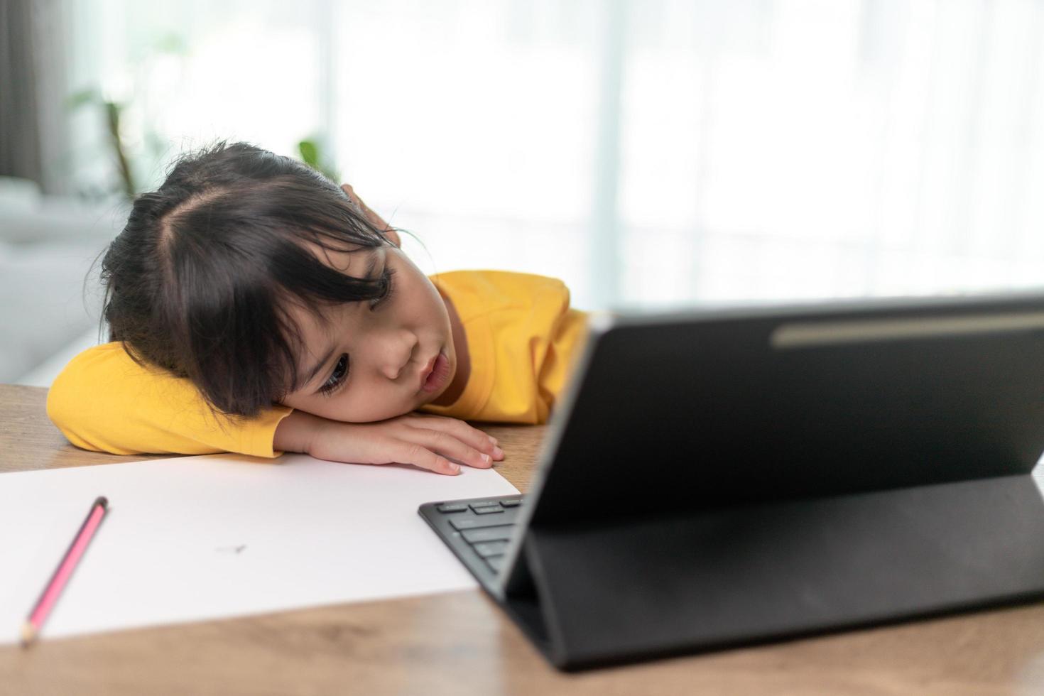 Little Asian girl sitting alone and looking out with a bored face, Preschool child laying head down on the table with sad  bored with homework, spoiled child photo