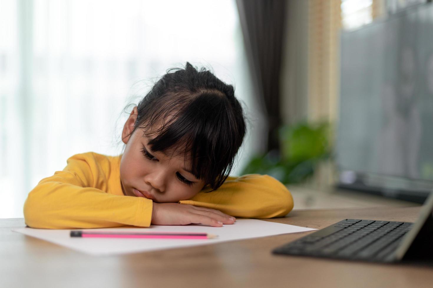 Little Asian girl sitting alone and looking out with a bored face, Preschool child laying head down on the table with sad  bored with homework, spoiled child photo