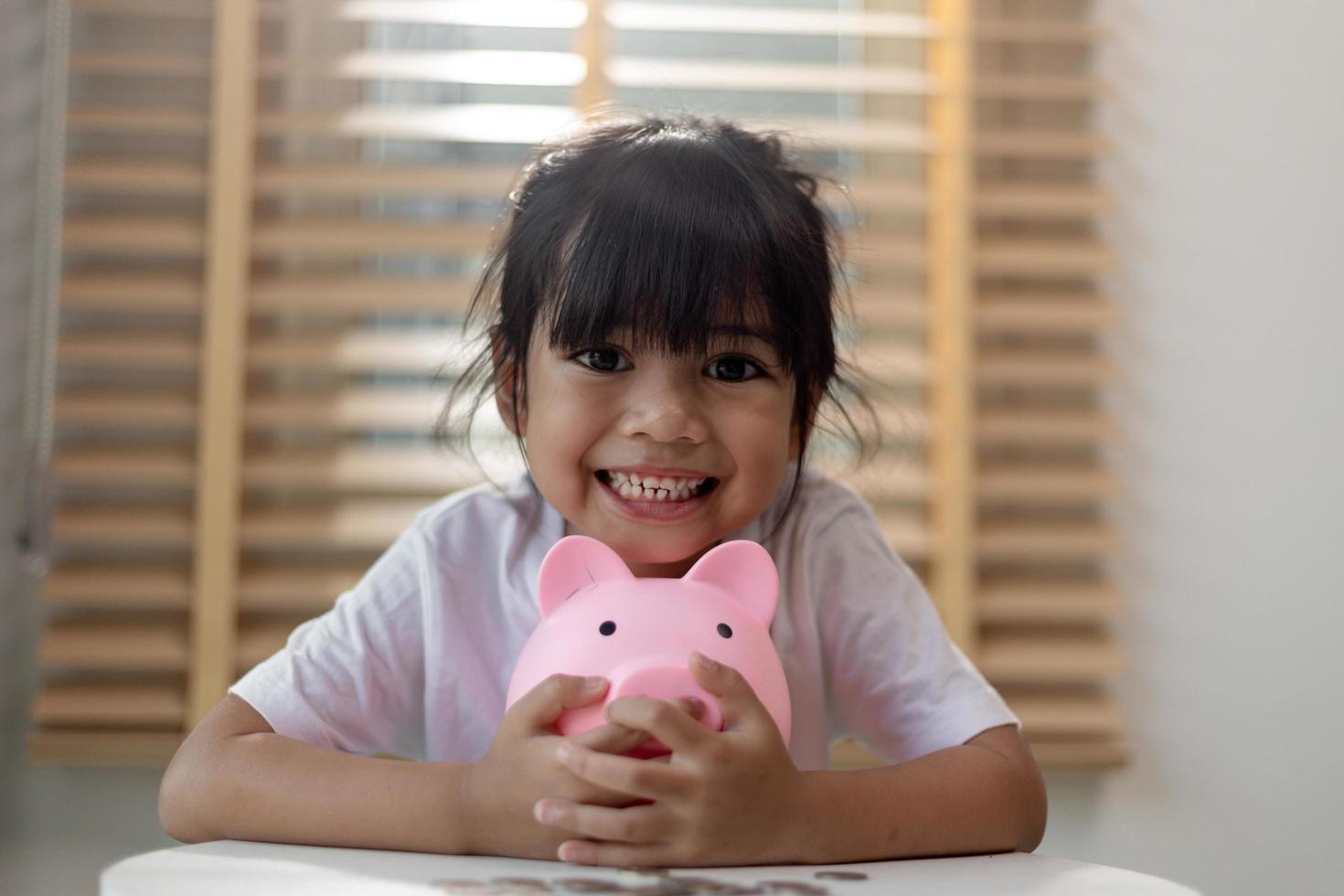 Little Asian girl saving money in a piggy bank, learning about saving, Kid save money for future education. Money, finances, insurance, and people concept photo