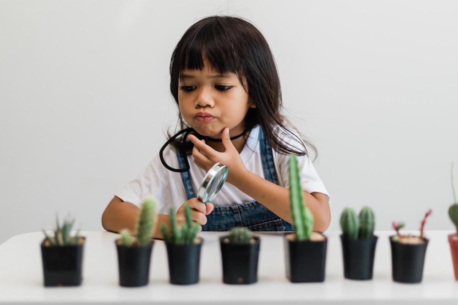 kid gently touch new stem of the cactus he grows with care, one hand holds magnifying glass.Nature education, Montessori and observation skills concept. photo