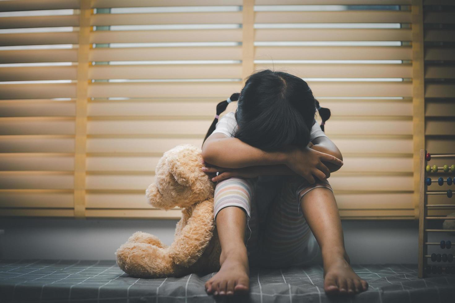 Close up lonely little girl hugging toy, sitting at home alone, upset unhappy child waiting for parents, thinking about problems, bad relationship in family, psychological trauma photo