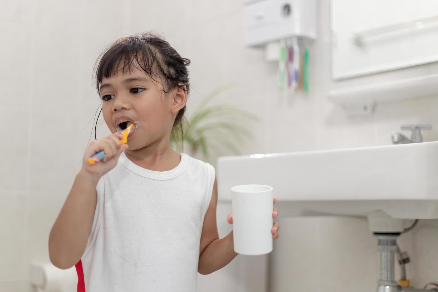 Little cute baby girl cleaning her teeth with a toothbrush in the bathroom photo