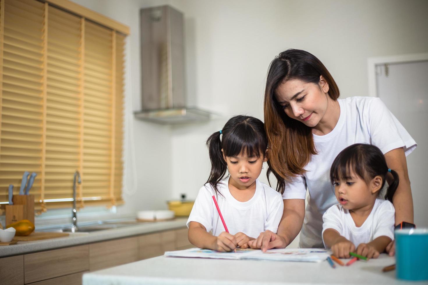 Happy mother and smiling daughter together painting using markers. Mother helping adopted child with art homework. Cheerful mother and asian little girl making painting at home. photo