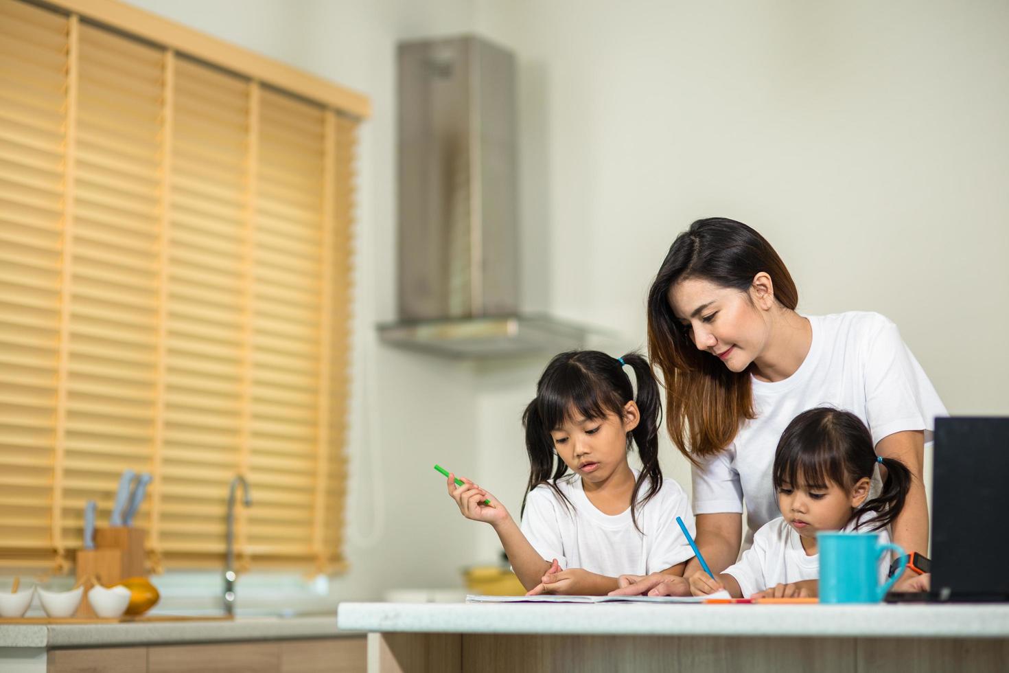 Happy mother and smiling daughter together painting using markers. Mother helping adopted child with art homework. Cheerful mother and asian little girl making painting at home. photo