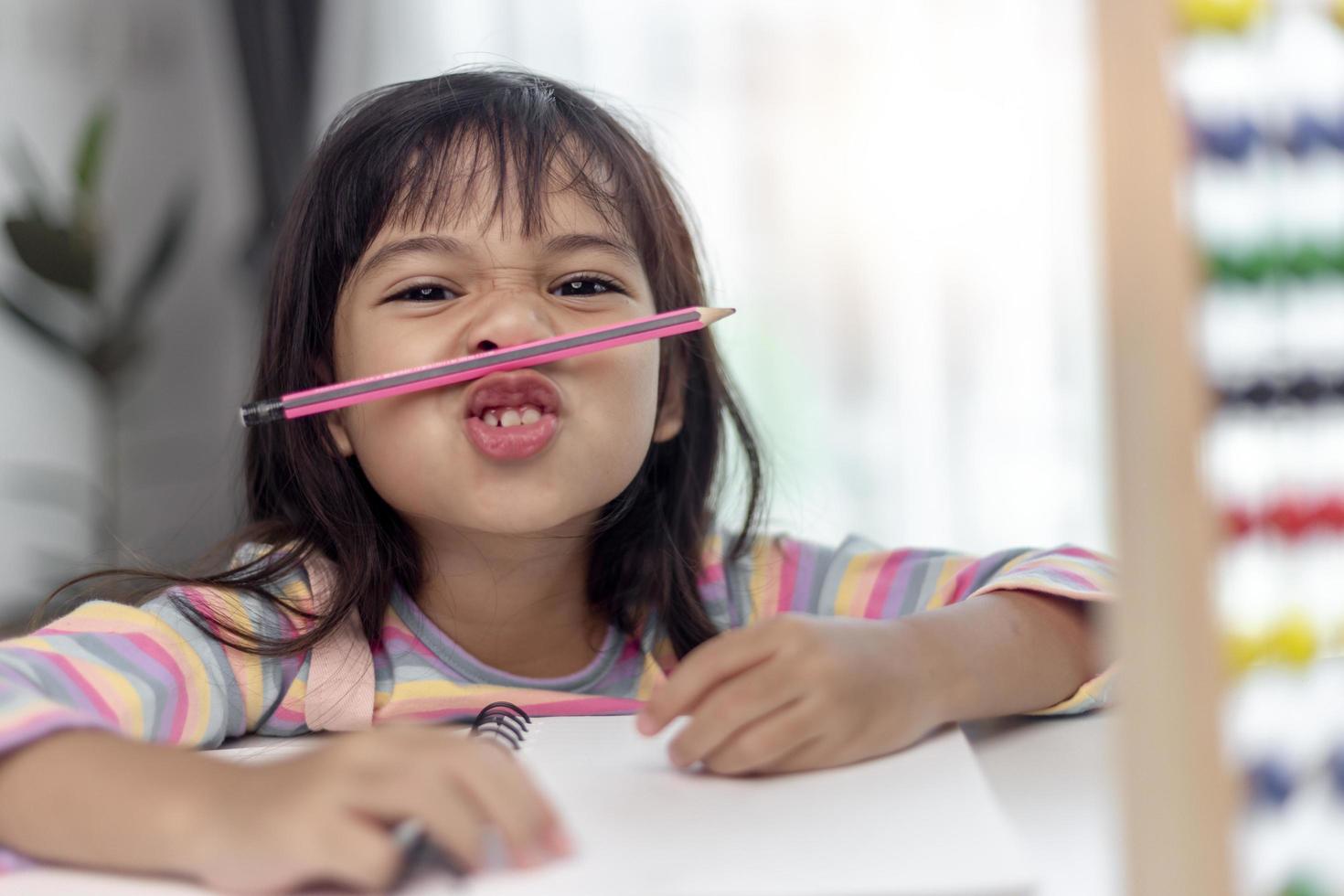 funny girl playing holding pen between nose and lips as mustache looking at the camera, playful bored after learning long hours. photo