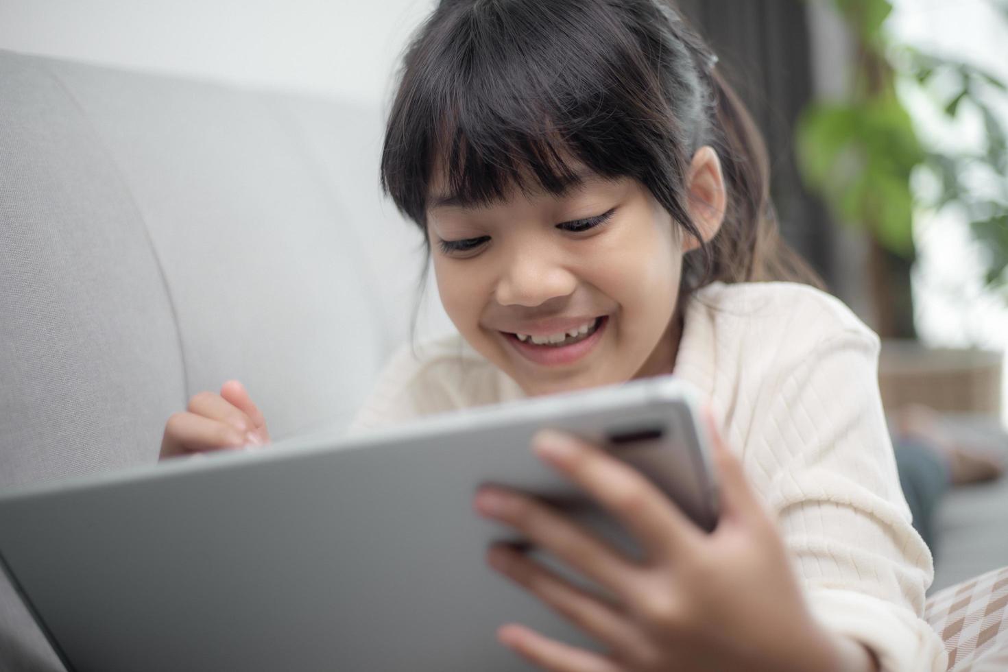 Little girl using tablet playing game on the internet, Kid sitting on sofa watching or talking with a friend online, Child relaxing in living room in the morning, Children with New Technology concept photo