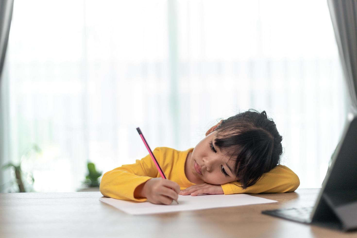 Little Asian girl sitting alone and looking out with a bored face, Preschool child laying head down on the table with sad  bored with homework, spoiled child photo