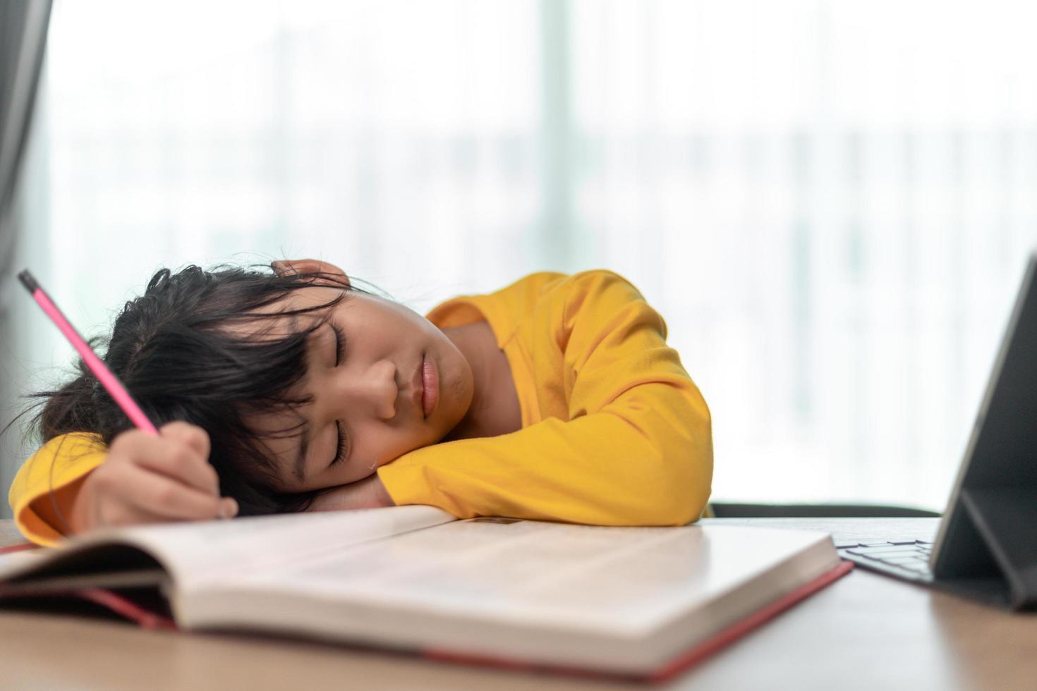 Little Asian girl sitting alone and looking out with a bored face, Preschool child laying head down on the table with sad  bored with homework, spoiled child photo